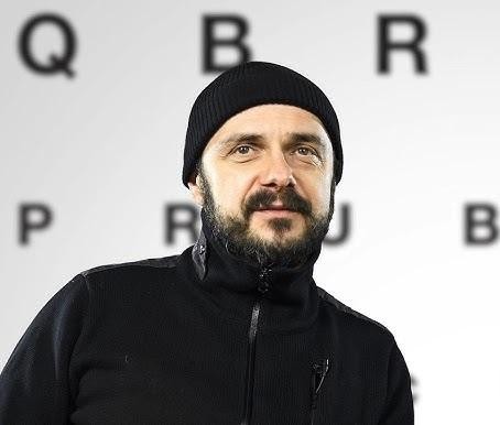 Arkadiusz Jakubik, wokalista zespołu Dr Misio, podczas energicznego występu na scenie, śpiewający do mikrofonu, z widocznymi członkami zespołu w tle.