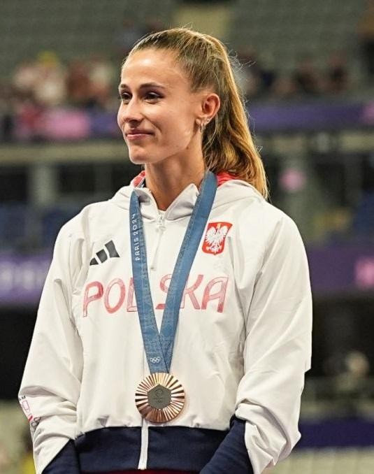 Natalia Bukowiecka w stroju sportowym, odpoczywająca lub rozciągająca się w naturalnym otoczeniu.