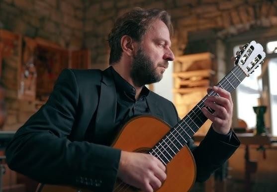 Zbliżenie na dłonie Marcina Dylli precyzyjnie grające na gitarze klasycznej, z widocznym napięciem strun i fakturą drewna instrumentu.