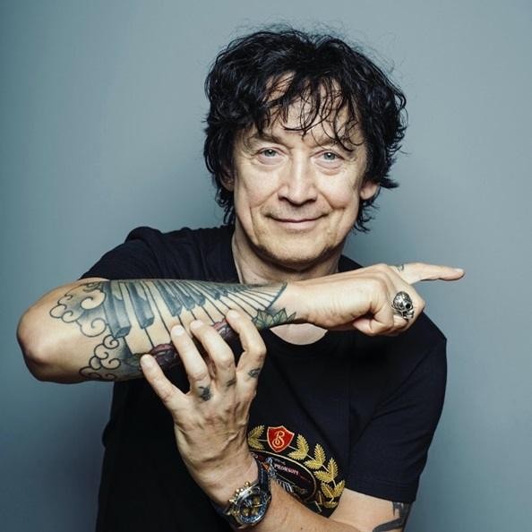 Jan Borysewicz na koncercie Lady Pank w Warszawie, grający na gitarze na tle rozświetlonej sceny, z widocznym w tle fragmentem publiczności lub charakterystycznym elementem miejskim.