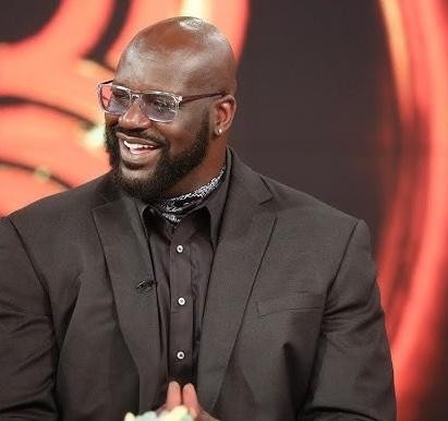 Shaquille O'Neal wykonujący wsad w koszulce Lakers (nr 34), ukazujący jego siłę i dominację na boisku, z rozmytym tłem areny NBA.